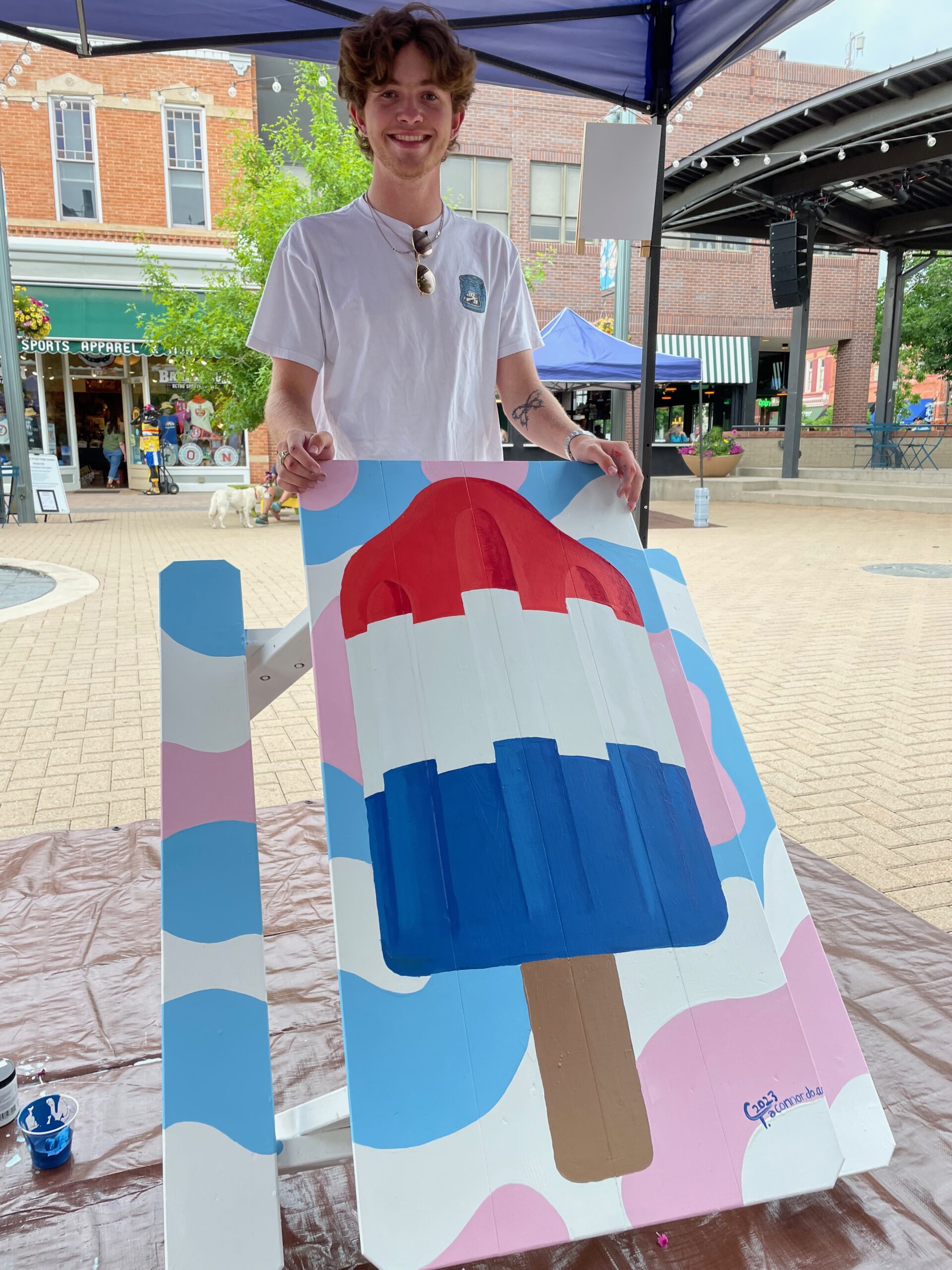 Man showcasing painted Adirondack table with a patriotic popsicle painting