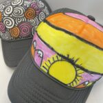 Two DIY trucker hats, one with a colored sunset, and the other geometric shapes