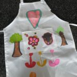 A colorful homemade apron, with images of trees, a heart and some flowers drawn on it.
