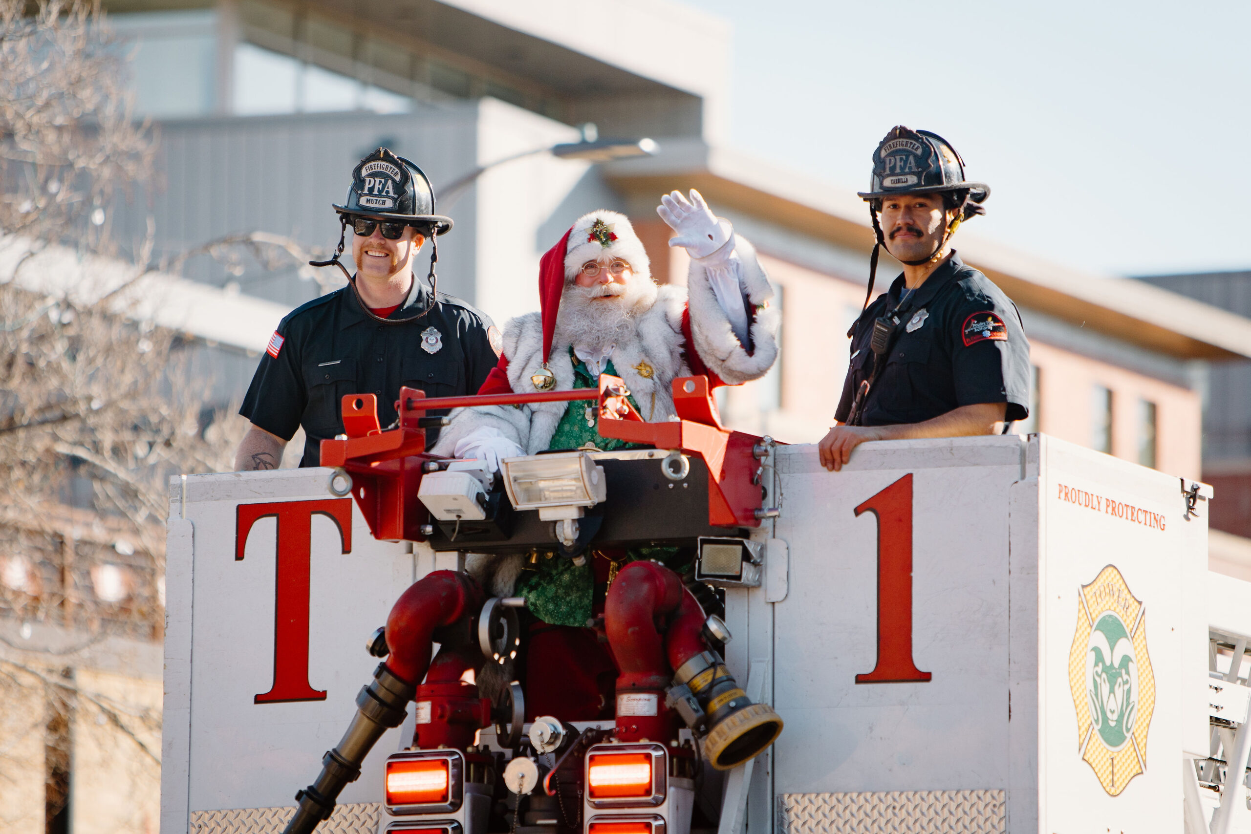 Santa, flanked by two firefighters, waves to the crowd from the top of a firetruck.