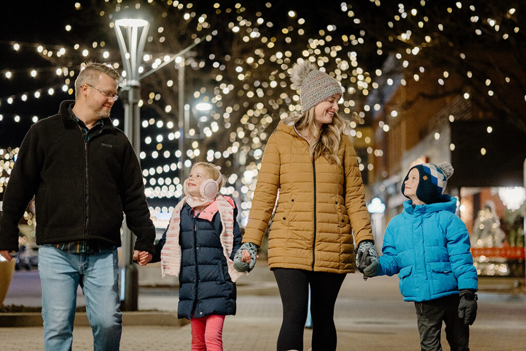 Family holding hands while walking in downtown fort collins during the winter under the twinkling holiday lights
